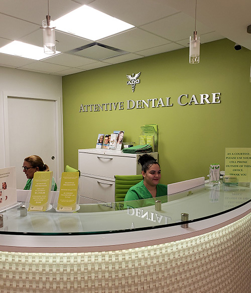 The image shows an interior view of a dental care office reception area with a sign indicating Attentive Dental Care on a green wall, a woman seated at the counter, and a desk with a computer monitor.