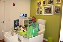 A man sitting at a desk with a computer monitor in front of him, wearing a white shirt and glasses.